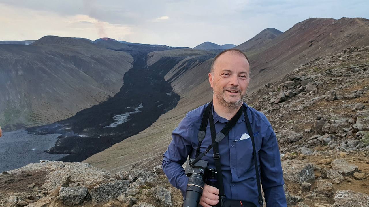 Portrait of Sylvain Bellier in a volcanic landscape, with a camera around his neck